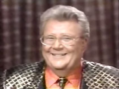 Rod is wearing a gold jacket with black squares, matching necktie & salmon shirt