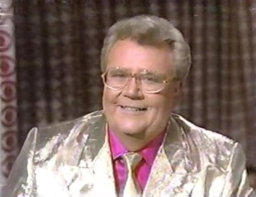 Rod is wearing a shiny yellow/yellow pinstriped jacket with matching tie and a purple shirt with matching pocket square