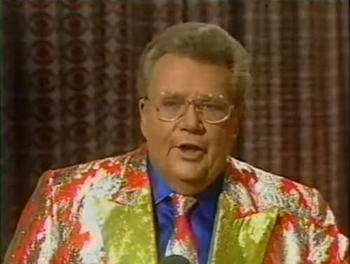 Rod is wearing a shiny orange jacket with silver oak leaves, gold lapel, matching necktie and a blue shirt