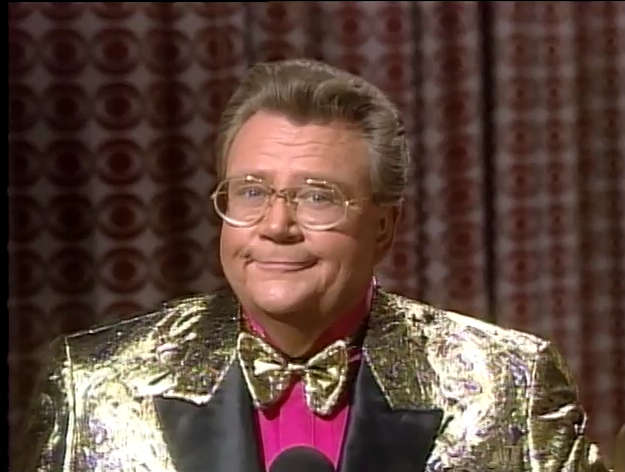 Rod is wearing a shiny gold jacket with black lapels, a matching bow tie & pink shirt