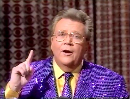 Rod is wearing a purple-sequined jacket, matching necktie & yellow shirt