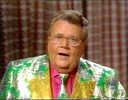 Rod is wearing a shiny green jack with silver oak leaves, gold lapels, matching neck tie & fuschia shirt