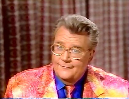Rod is wearing shimmery peach/yellow/pink gradient jacket, matching tie & blue silk shirt