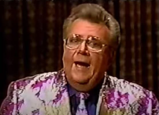 Rod is wearing a shiny purple jack with silver leaves & gold lapels with matching tie & dark-blue shirt