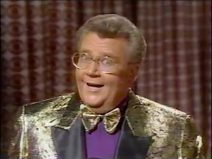 Rod is wearing a gold-patterned jacket with black lapels, matching bowtie & a purple shirt