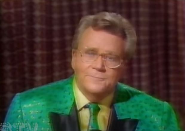 Rod is wearing a shiny green w/ green splotches jack with black lapels, matching tie and a yellow shirt