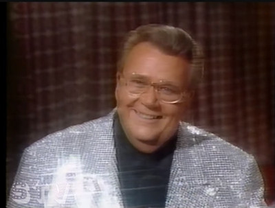 Rod is wearing a silver sequined jacket & black collarless silk shirt