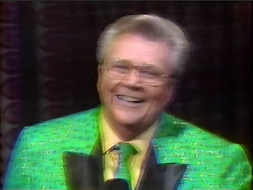 Rod is wearing a green jacket with shiny specks, black lapels and matching necktie & a yellow shirt with matching pocket square