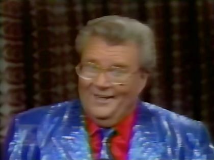 Rod is wearing a shiny blue/blue-striped jacket, matching necktie and red silk shirt