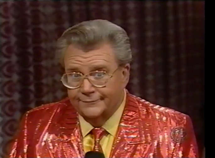 Rod is wearing a shiny red/red-striped jacket, matching necktie & yellow shirt
