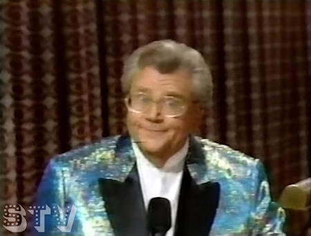 Rod is wearing an iridescent jacket with black lapels & white collarless shirt