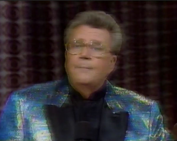 Rod is wearing a shiny iridescent jacket with black lapels & black collarless silk shirt
