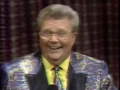 Rod is wearing an iridescent-silver jacket with black lapels, matching necktie & yellow silk shirt