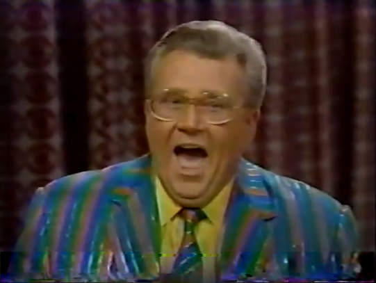 Rod is wearing a shiny blue/green/pink jacket, matching tie & yellow shirt