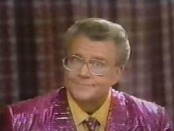 Rod is wearing a shiny purple/purple-striped jacket & tie with yellow shirt