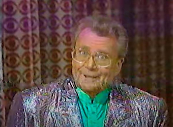 Rod is wearing a shiny-silver jacket & green silk collarless shirt