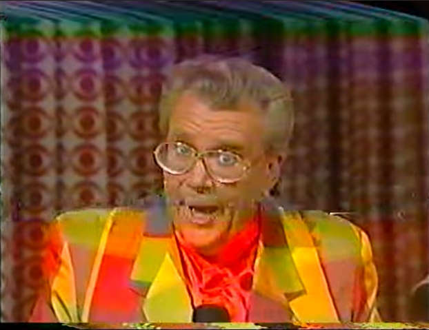 Rod is wearing a jacket with red-orange-yellow-green squares & red collarless silk shirt