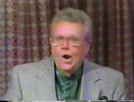 Rod is wearing a grey jacket & dark-green collarless silk shirt with matching pocket square