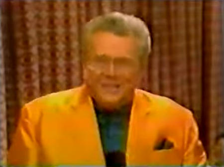 Rod is wearing an orange jacket & dark-green collarless silk shirt with matching pocket square