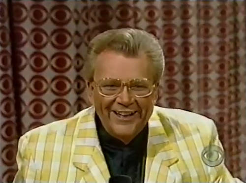 Rod is wearing a yellowish gingham jacket & black collarless silk shirt