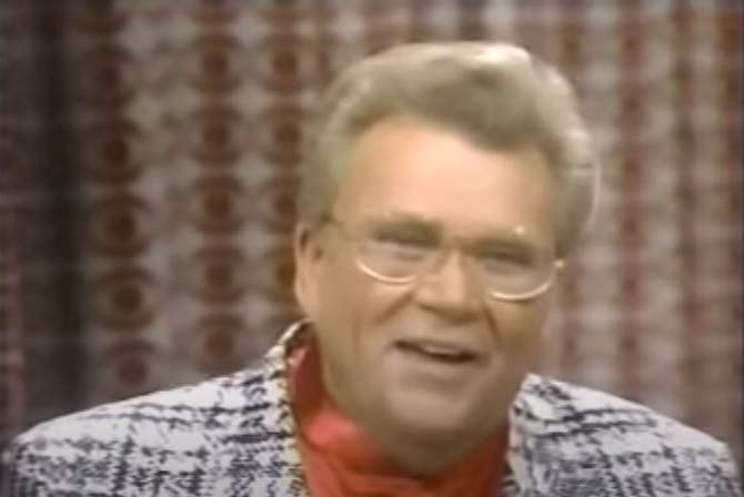 Rod is wearing a houndstooth/plaid jacket & salmon-colored silk collarless shirt